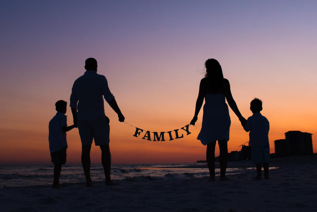 silhouette portrait of the family of four with the family sign during colorful sunset