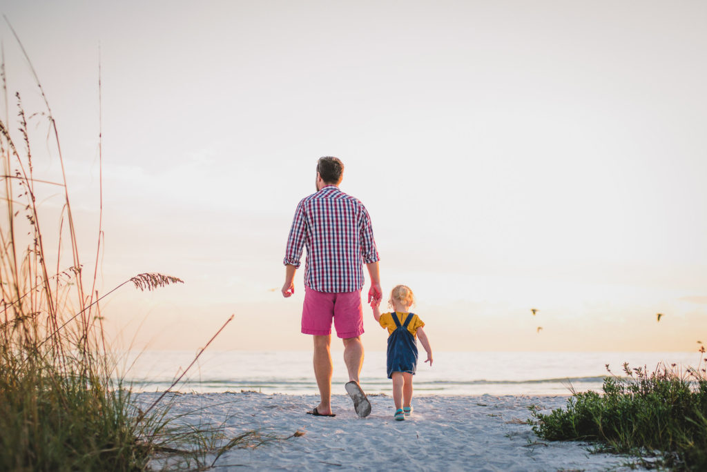 father with small daughter walking at the beach during sunset