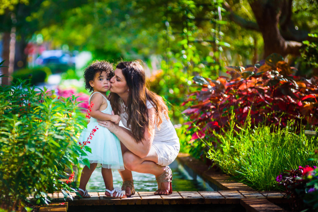 mom kissing daughter in a cheek in flowers garden