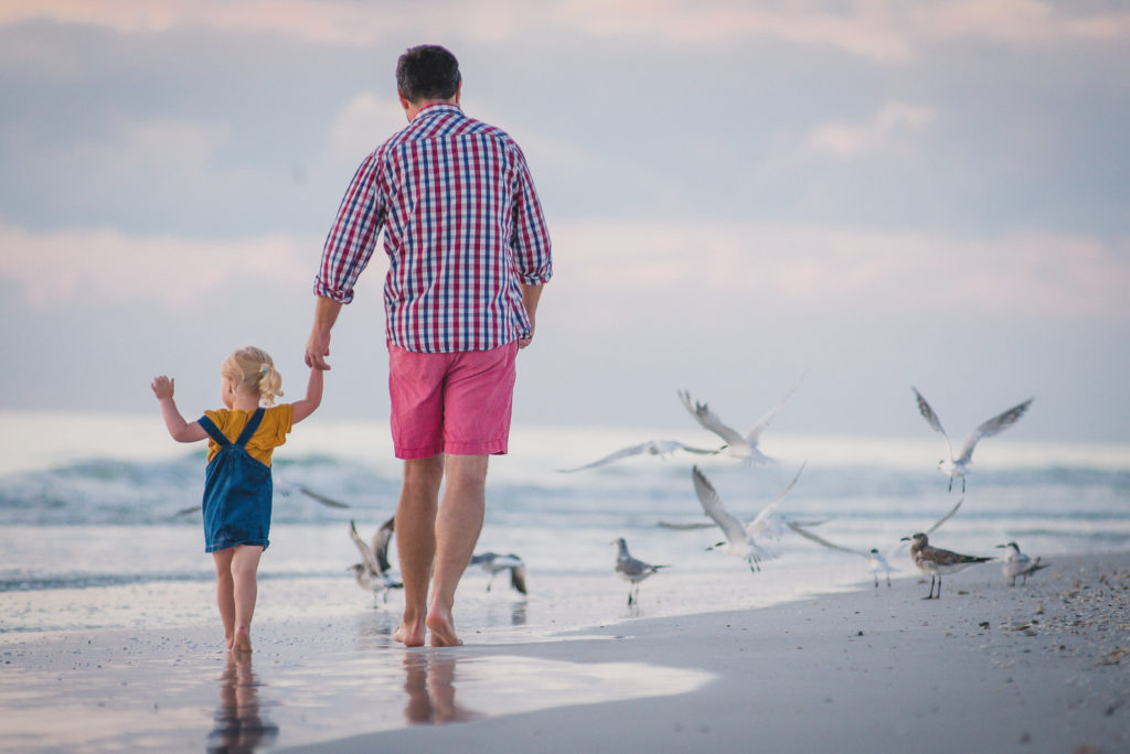 father and daughter walking the beach at water edge