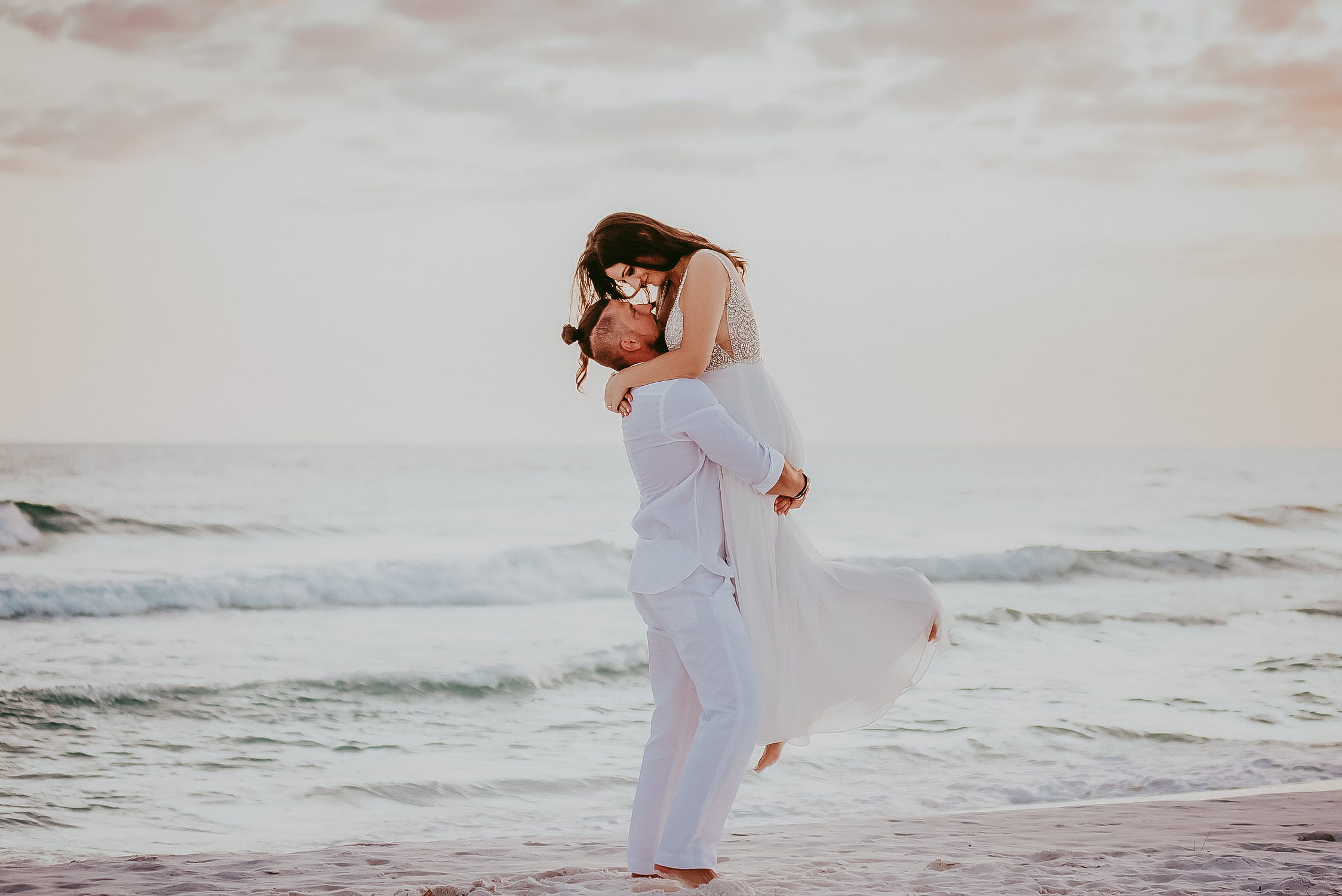 groom picking up bride and looking in her eye at the beach