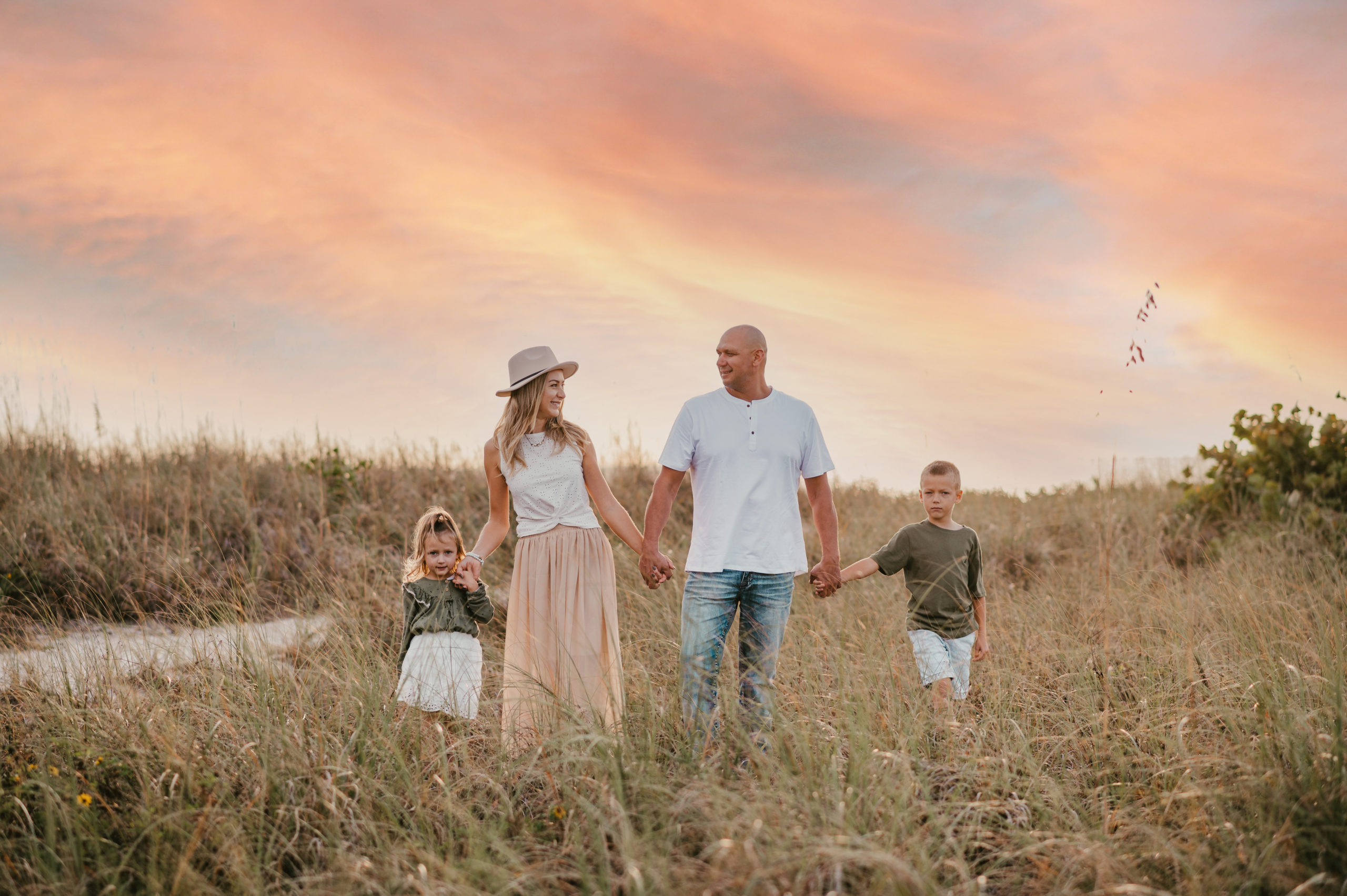 Family holding hands and standing in tall grass posing for family pictures during sunset