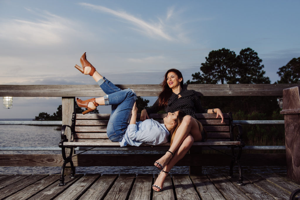 two fiends having amazing time, laughing on a bench in front of a lake.