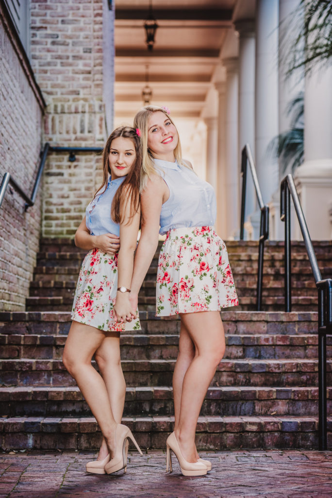 Two girls in floral skirts posing on steps.