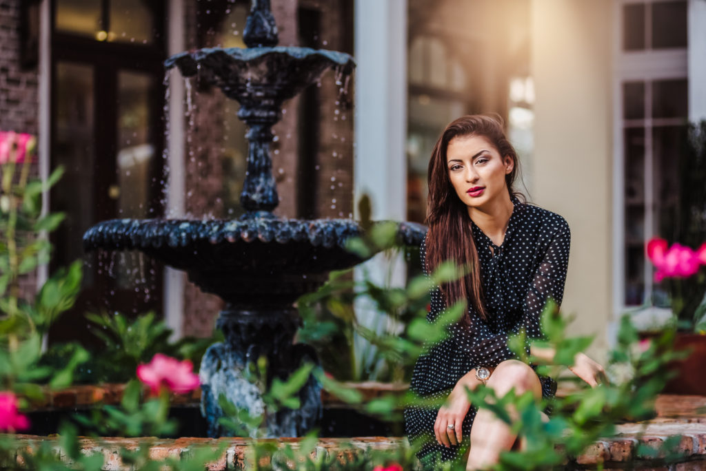 A high school senior girl sitting on a fountain in front of flowers in Sarasota garden