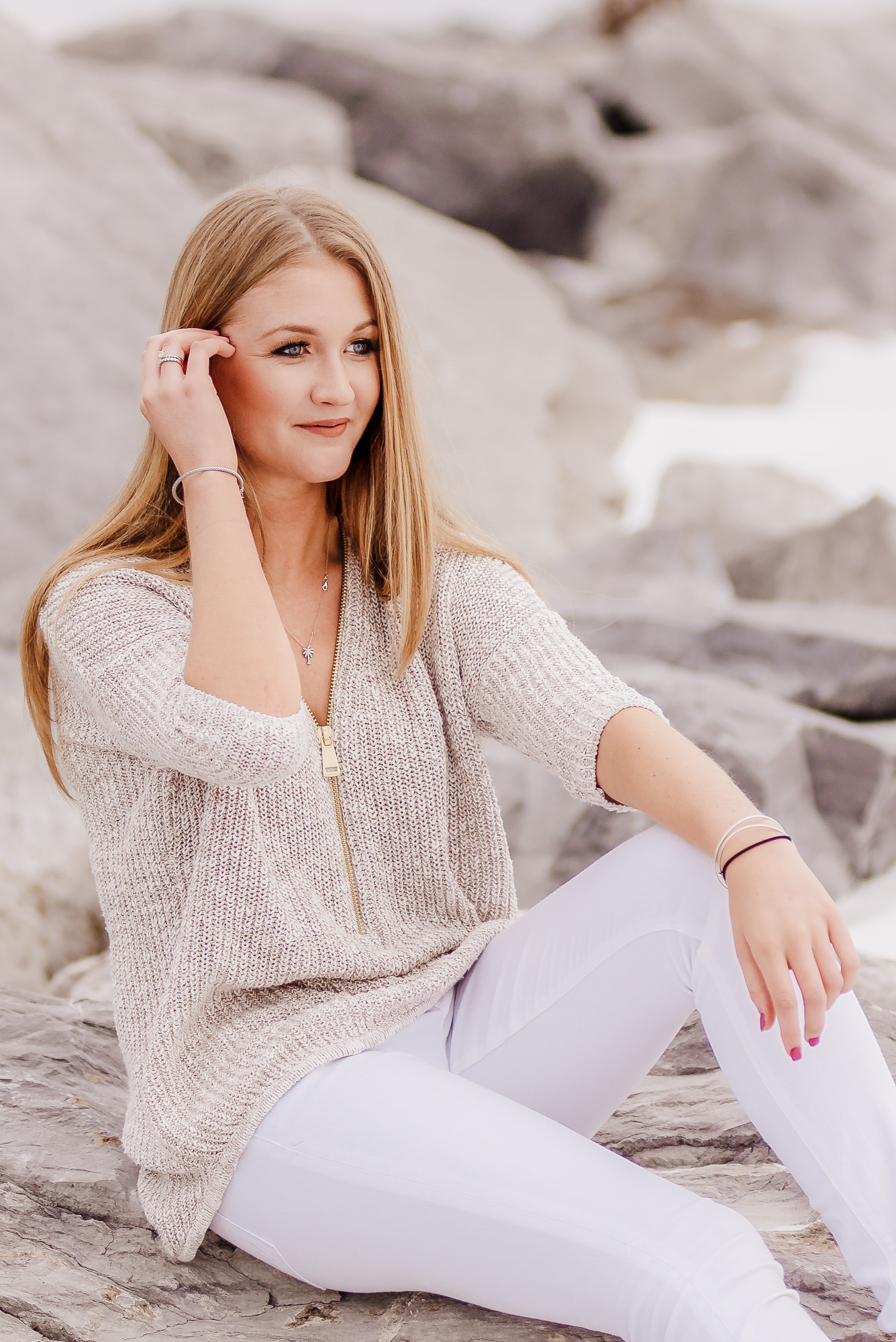 A portrait of beautiful young woman sitting on rocks with a sweater and jeans.