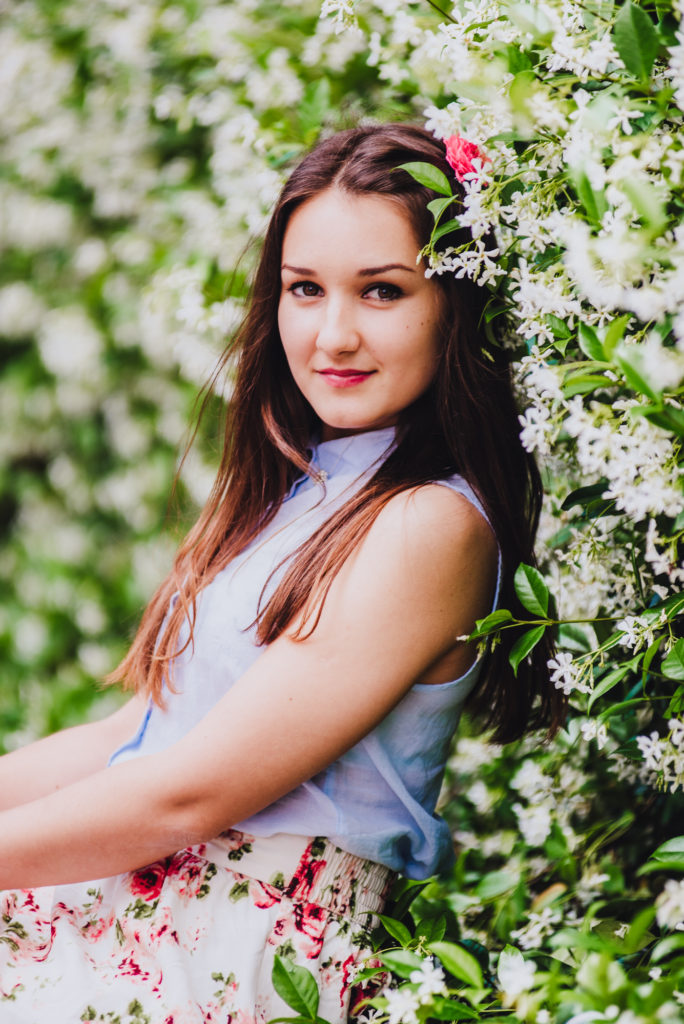 A girl posing in front of a bush with white flowers for her senior portraits