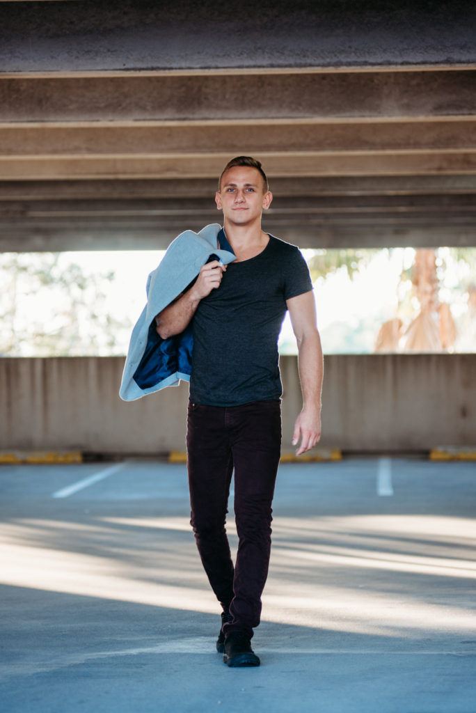 A senior guy walking under an overpass with a jacket.