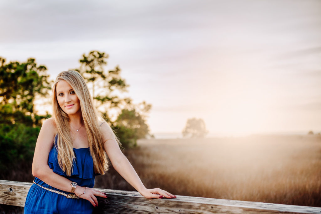 beautiful girl with long hair posing for her hoigh school senior portrait in Folrida tall gras during the sunset session