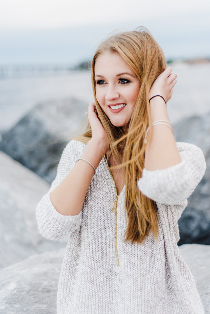 A close up of young woman wearing a sweater is posing on rocks at Sarasota beach for her senior portraits