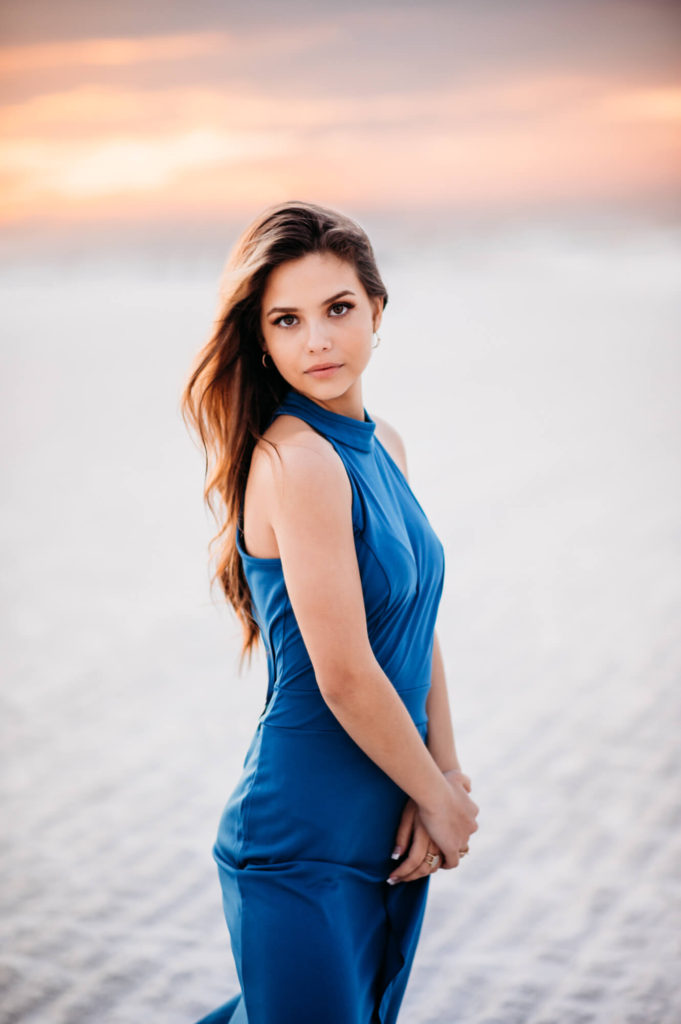 A beautiful young woman in a blue dress standing on the Siesta beach at sunset.
