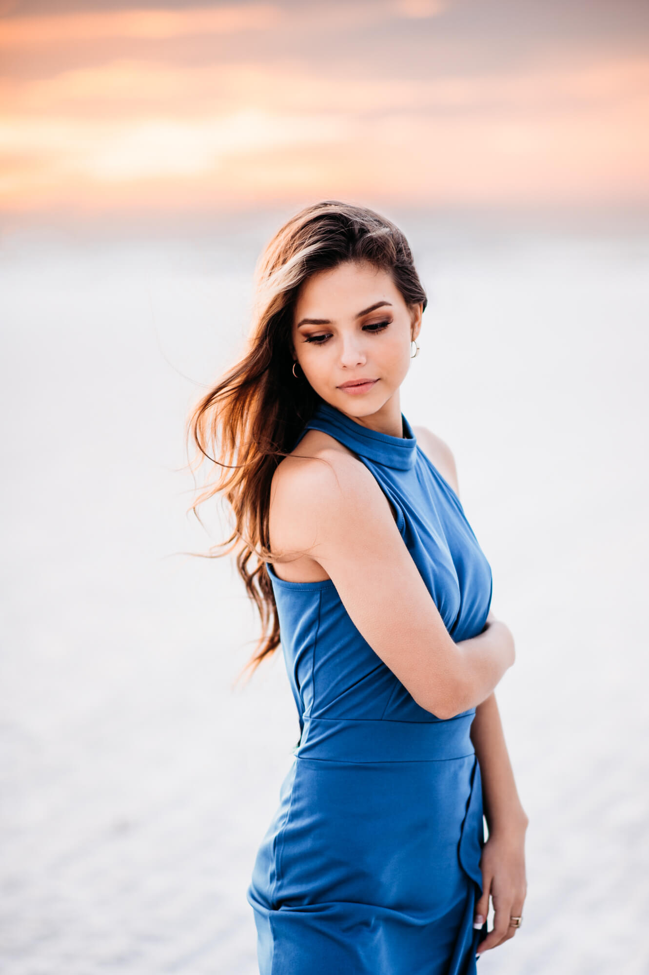 A woman in a blue dress standing on the beach at sunset during high school senior photoshoot