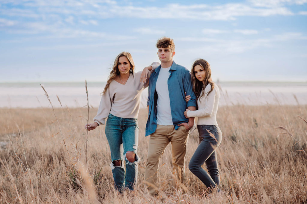 Three young high school seniors standing in a field of tall grass.