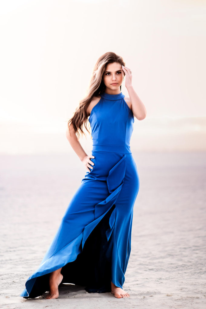 A woman in a blue dress posing on the beach for her senior portraits