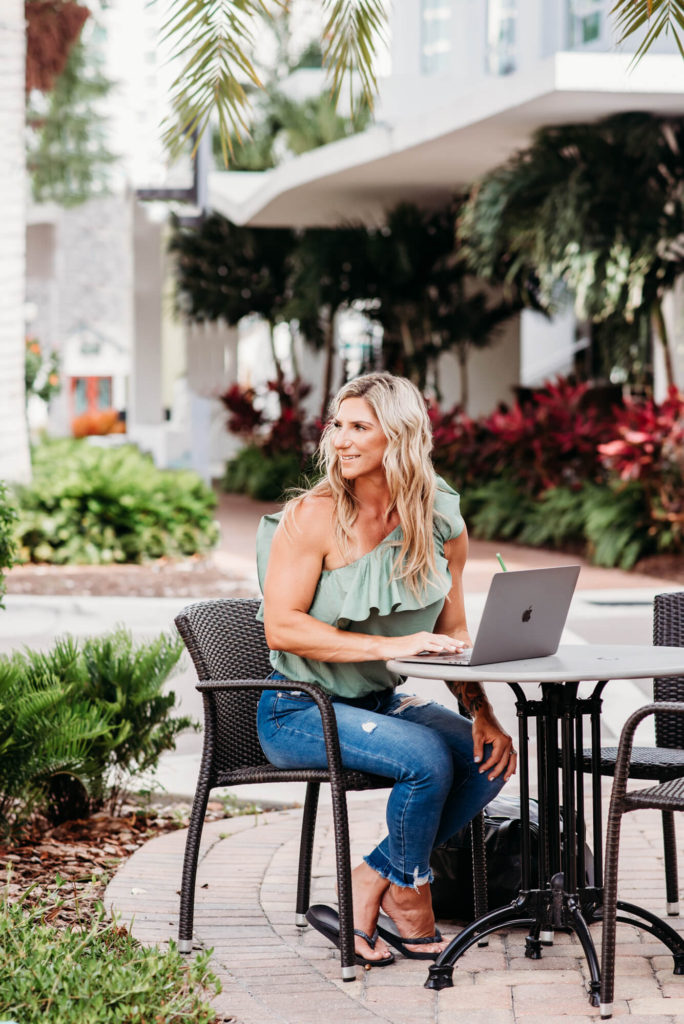 A fitness and Health Coach sitting at an outdoor table with a laptop.