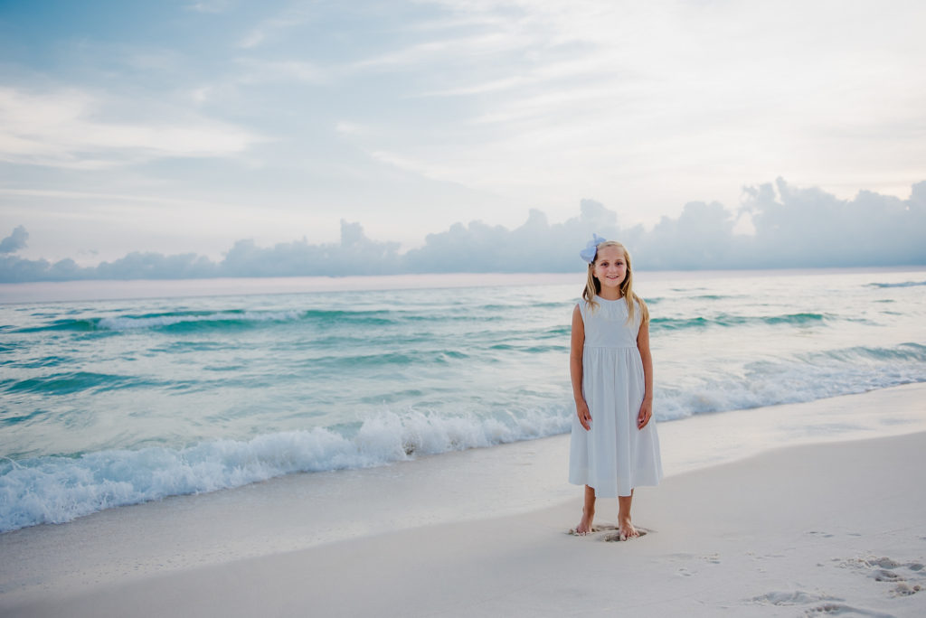 Portrait of little girl wearing white dress at the white sand Siesta Key beach with emerald color water as the background