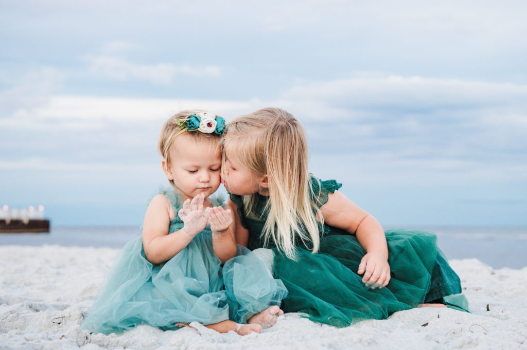 beach portrait of one sister kissing her little sister