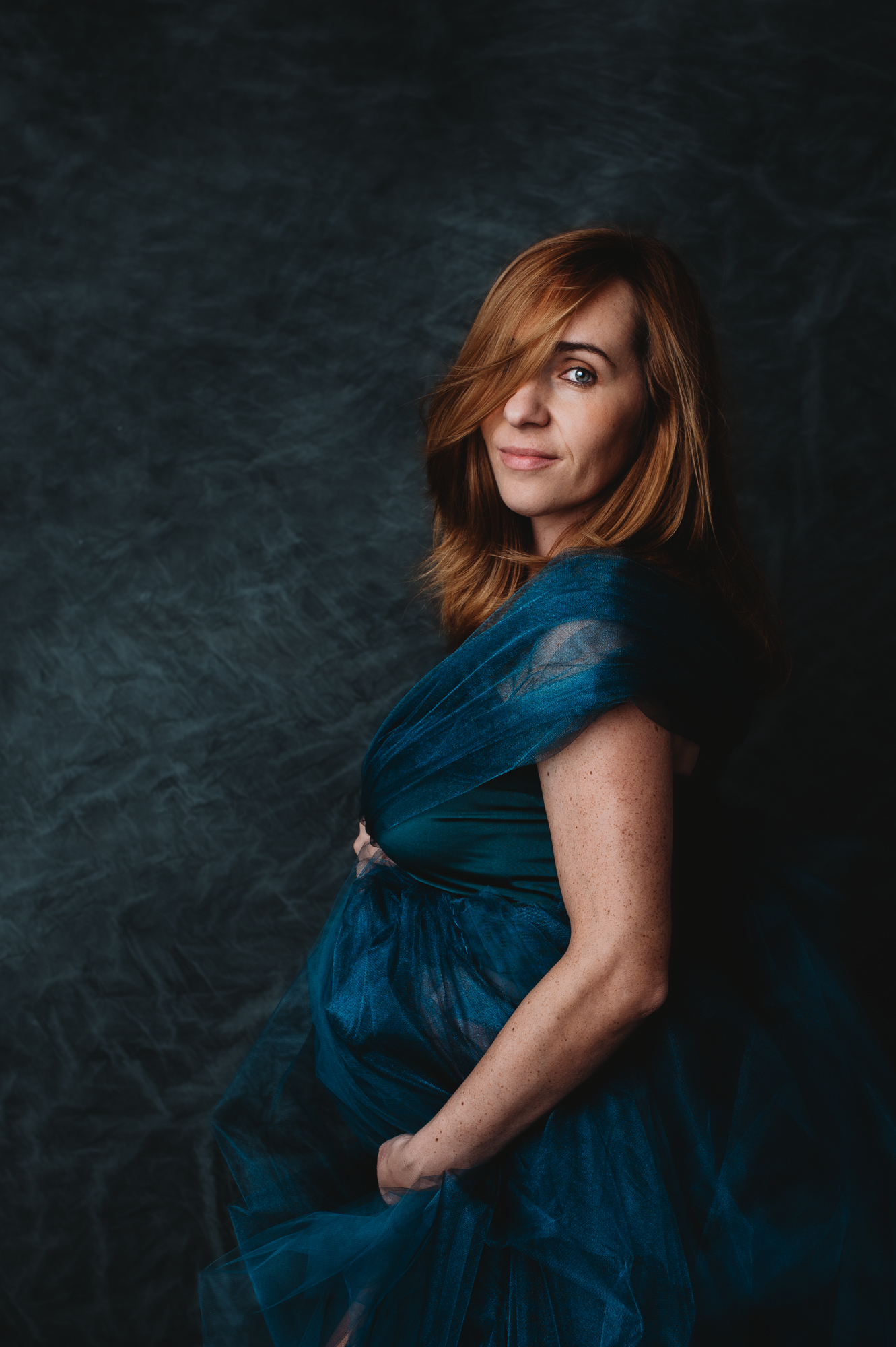 Beautiful redhead pregnant women in deep green tule dress posing for maternity session in Sarasota portrait studio