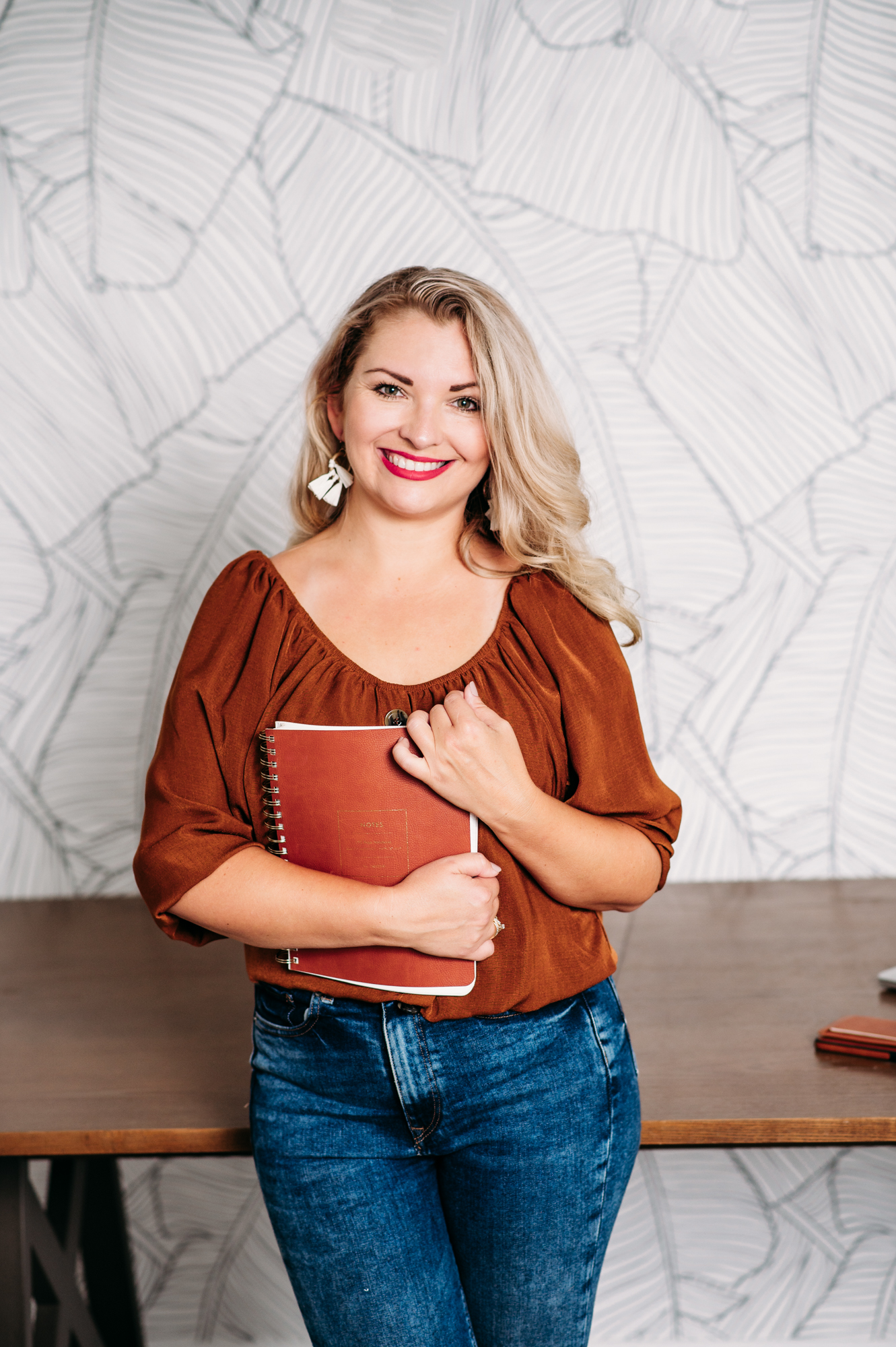 Lifetime personal branding portrait of standing with notebook in her hands and smiling  life coach in the bright office.