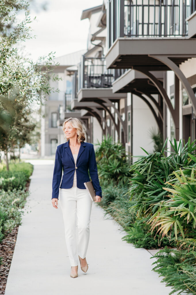 A life coach in a blue blazer and white pants walking on the sidewalk for lifestyle headshot, personal branding photography in front of apartment buildings.