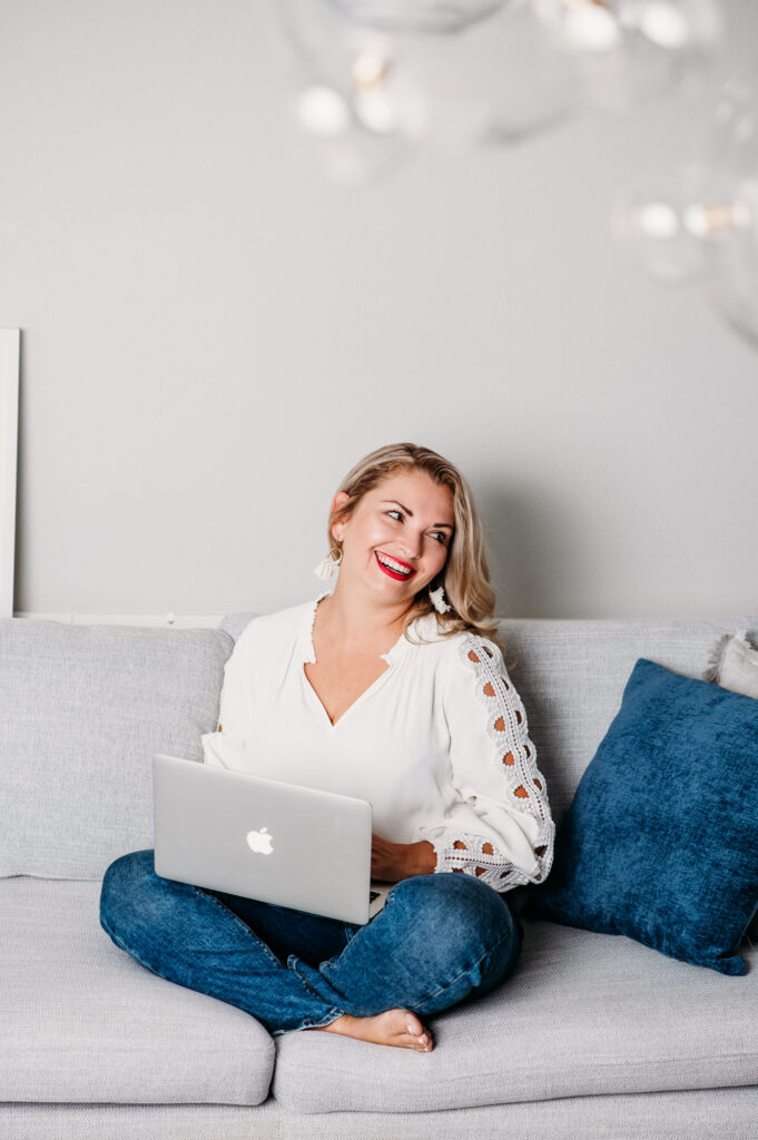 A woman, engaged in a personal brand photoshoot, is sitting on a couch with a laptop.