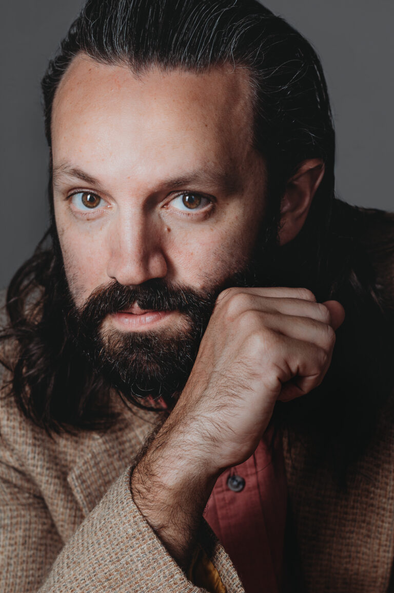 modern close up headshot of a man with long hair and beard looking at the camera