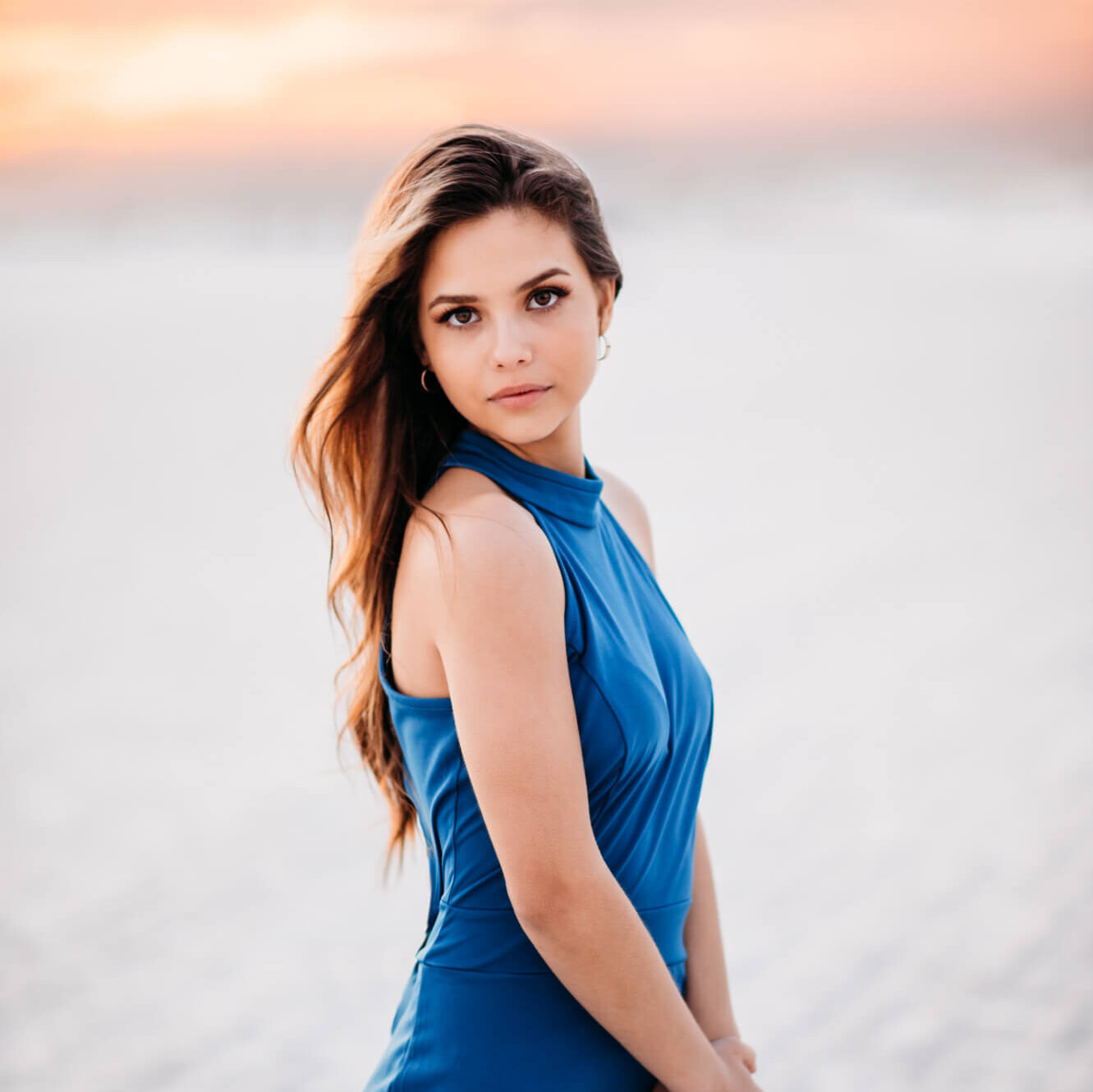 A young woman in a blue dress standing on the Siesta Beach beach at sunset for her senior portrait