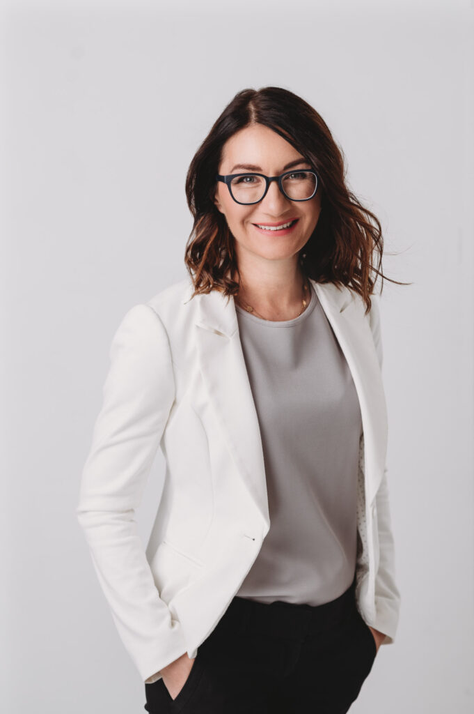 Modern headshot of dark hair women wearing white jacket on light gray background smiling into camera