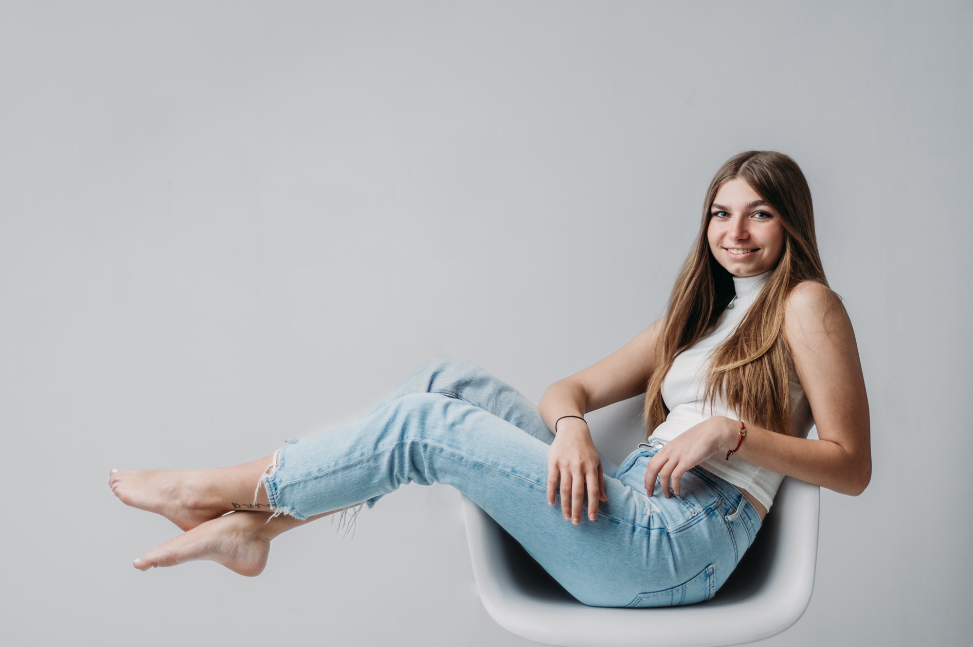 studio portrait of a high school student wearing blue jeans and white top on light gray backdrop