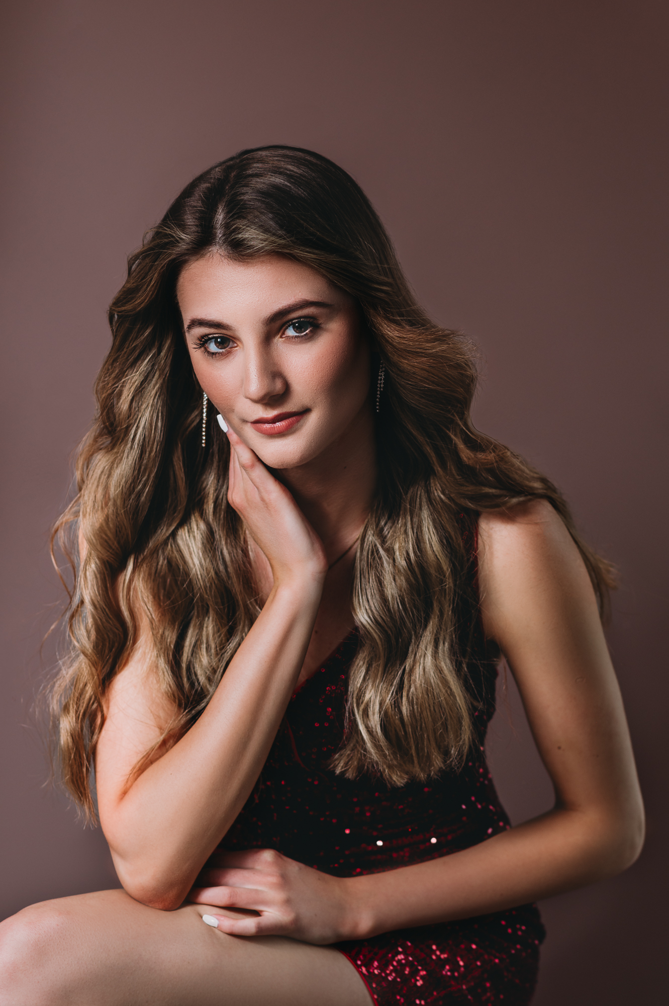 A beautiful young woman posing in a red dress at a portrait studio.