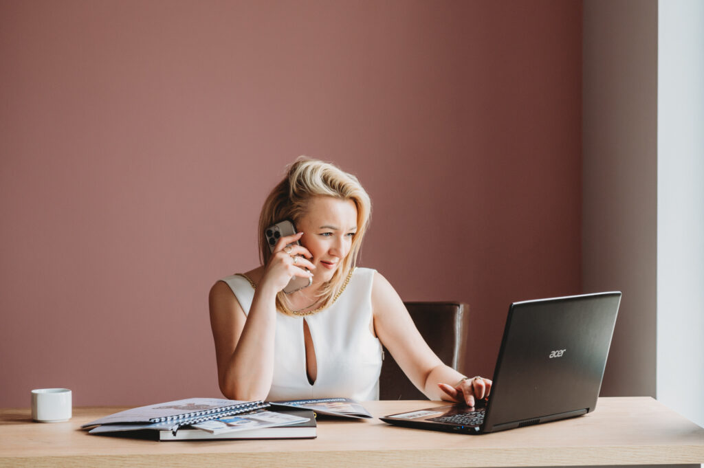 A professional portrait of a woman at her desk with a cup of coffee and a laptop.