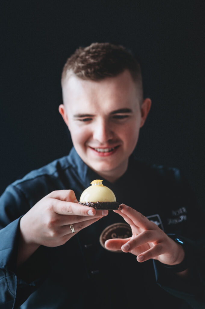 A business portrait of a professional chef holding a desert on the black background