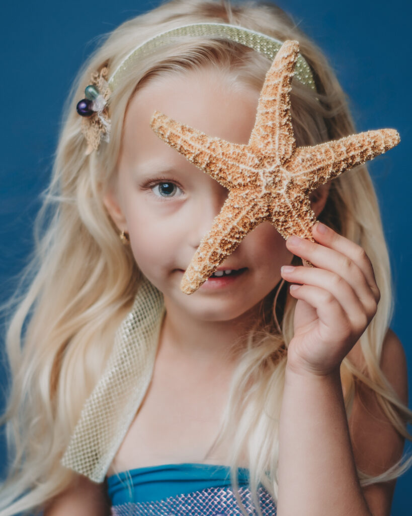 A little girl holding a starfish on a blue background.