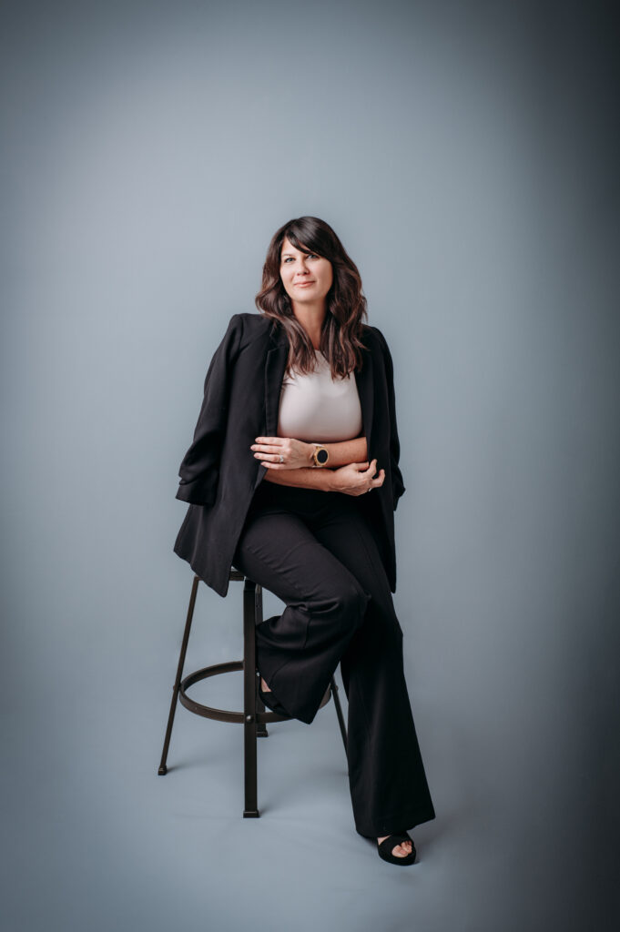 A full body shot of a woman posing for a professional headshot on a stool