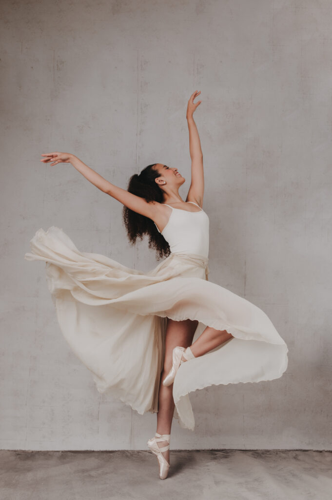 A ballerina in a light dress dances on a gray background at Sarasota studio