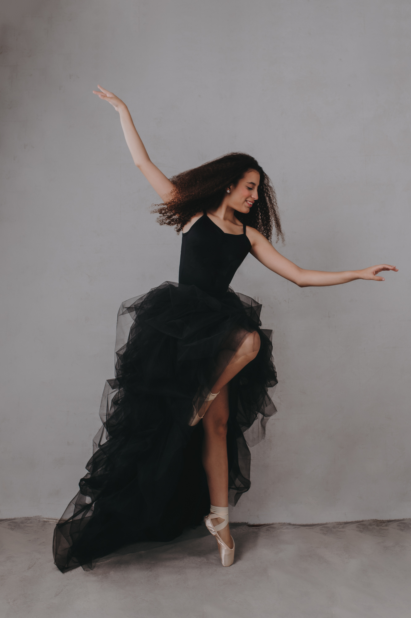 A ballerina in a black tutu dances on a gray background at Sarasota studio