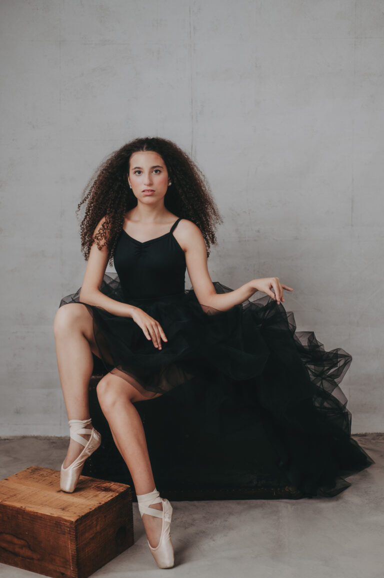 A young woman in a black dress sitting on a box.