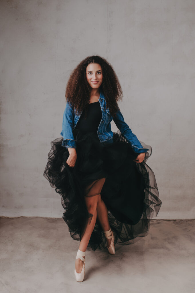 A young woman in a black dress posing in front of a gray background.