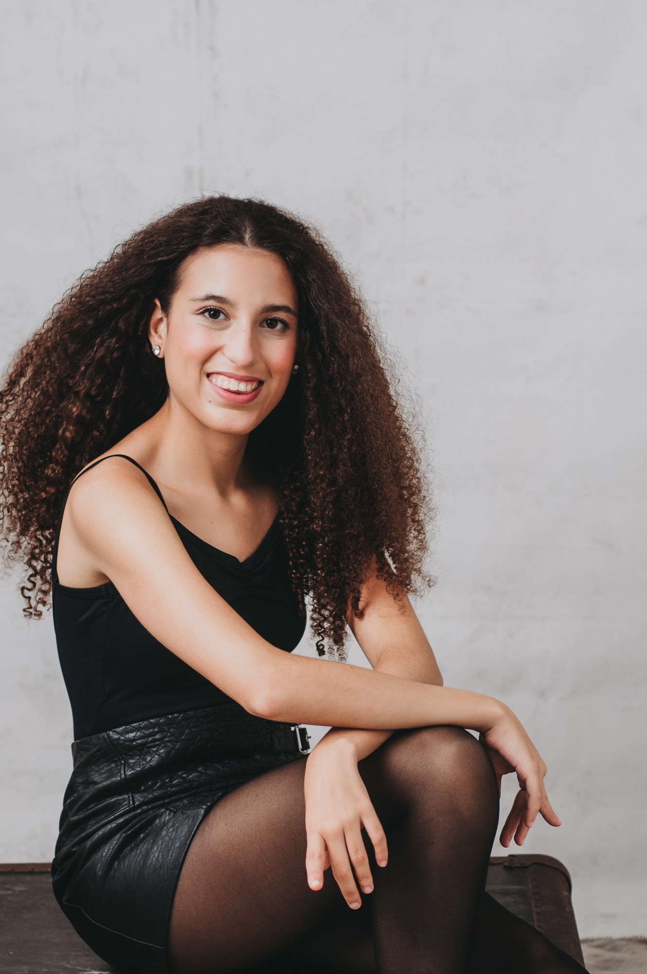 Relaxing headshot of A young woman with curly hair sitting on a chair.