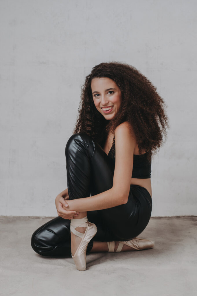 A young woman in black leather pants and baller shoes sitting on the floor