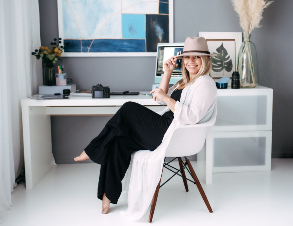 A senior photographer capturing a woman in a hat for her senior portrait sitting in front of a desk.