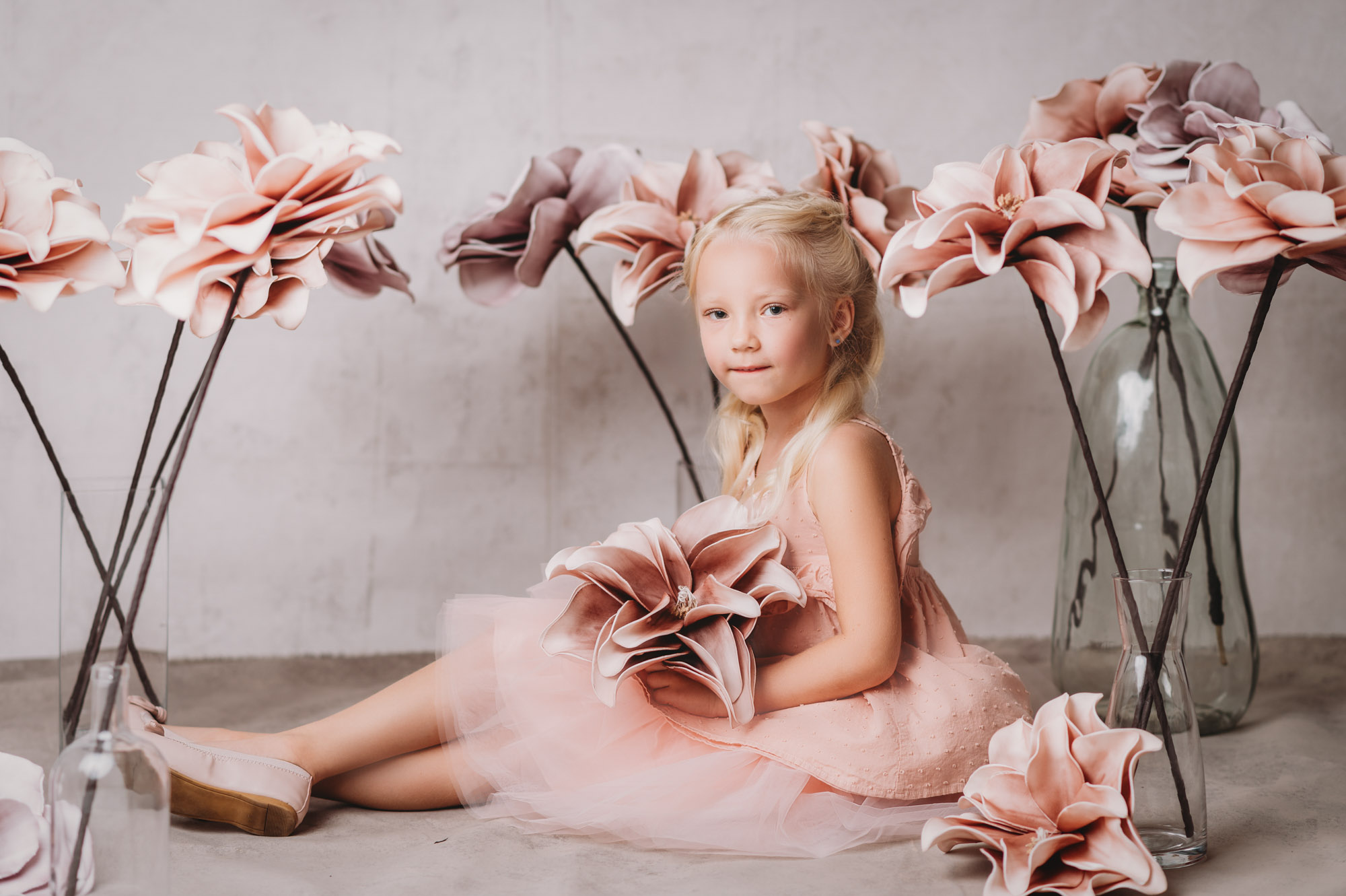 A little girl in a pink dress sitting on the ground with flowers, captured by a Sarasota photographer.