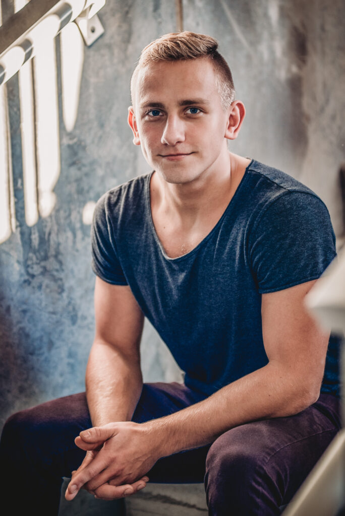 A young man in a blue shirt posing for his senior portrait on a staircase.