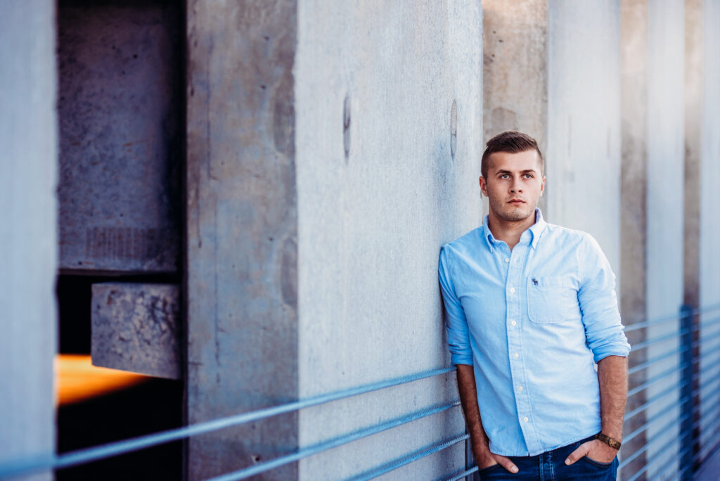 A young man posing for his senior picture, leaning against a railing.