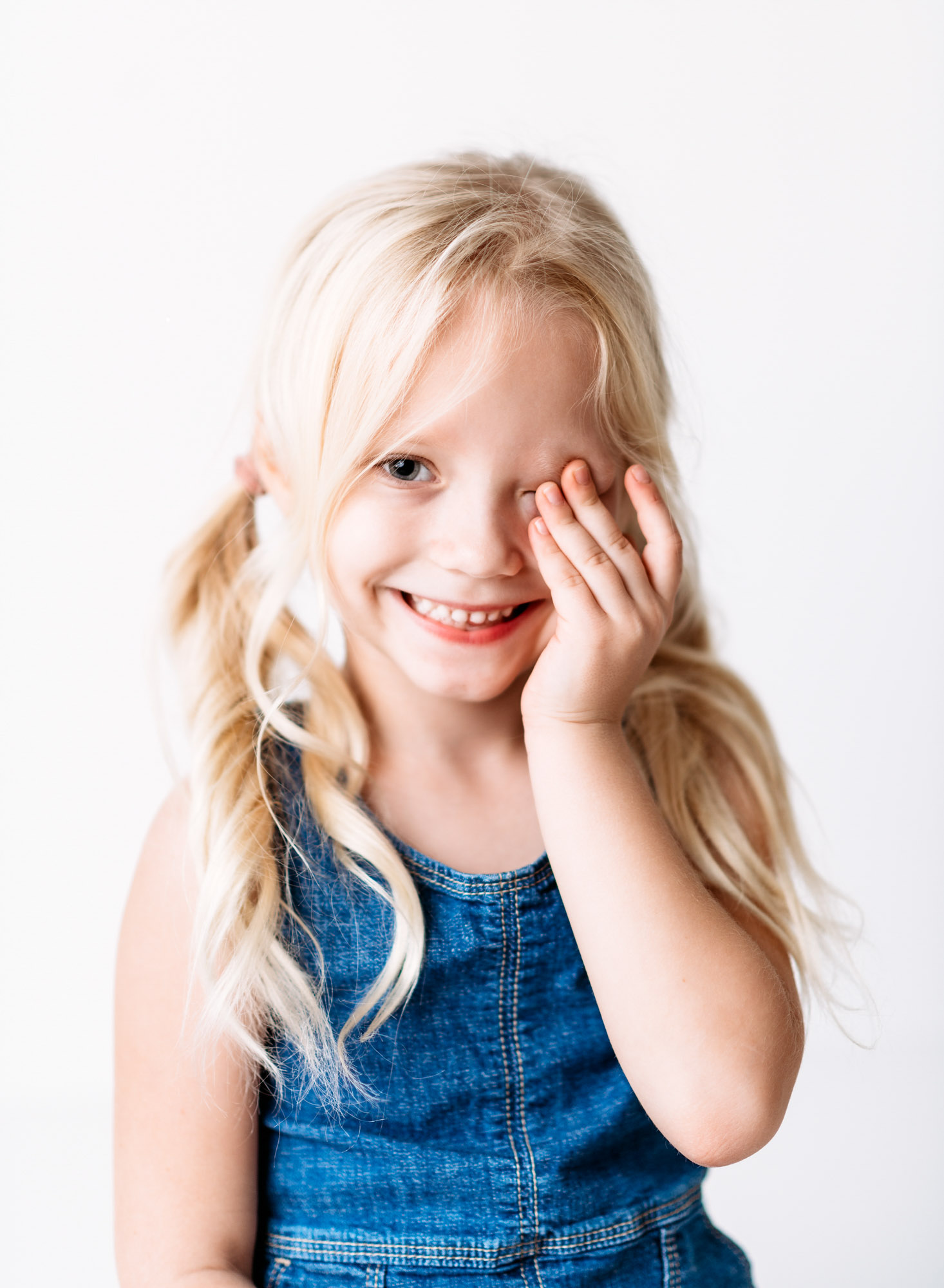 A sarasota photographer captures a little girl in a denim dress with her hand on her face.