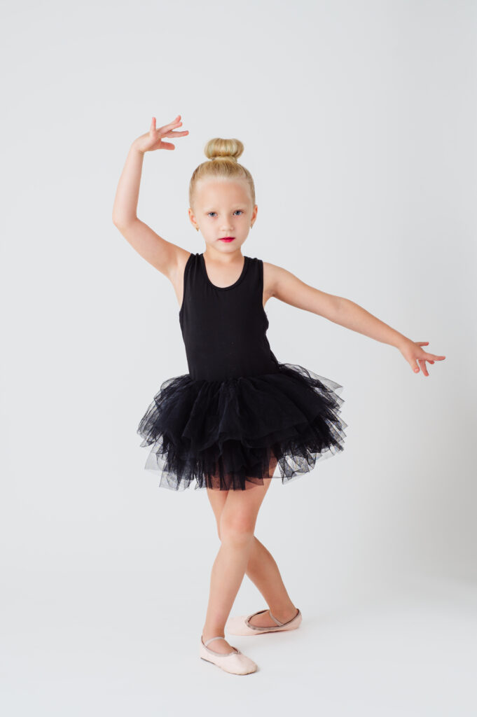 A little girl in a black tutu posing on a white background.