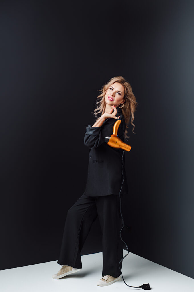 A hairstylist holding a hairdryer in front of a black background, showcased in Sarasota personal branding photography.