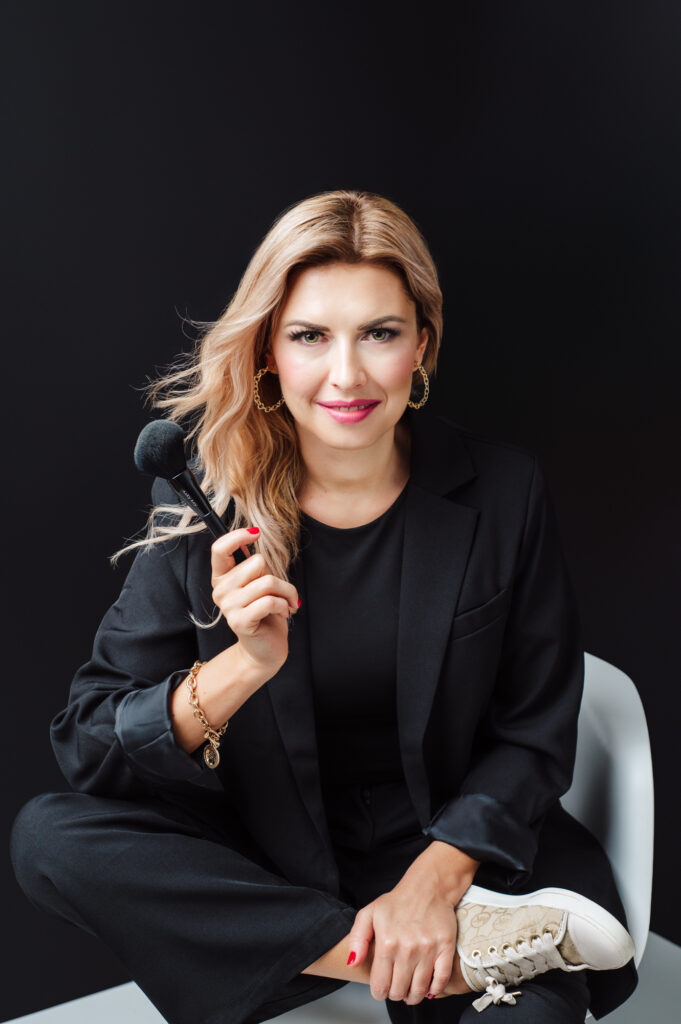 A woman in Sarasota, captured by a skilled personal branding photographer, is gracefully seated on a chair while delicately holding a makeup brush.