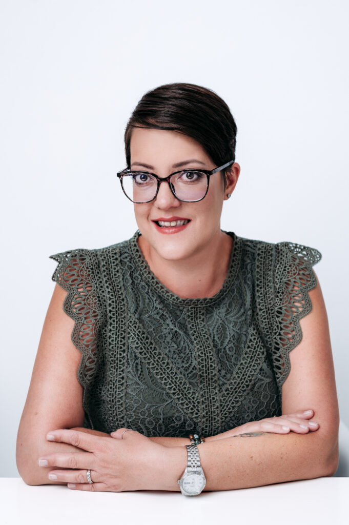 A professional portrait of social media specialist in glasses sitting at a table for personal branding photography.