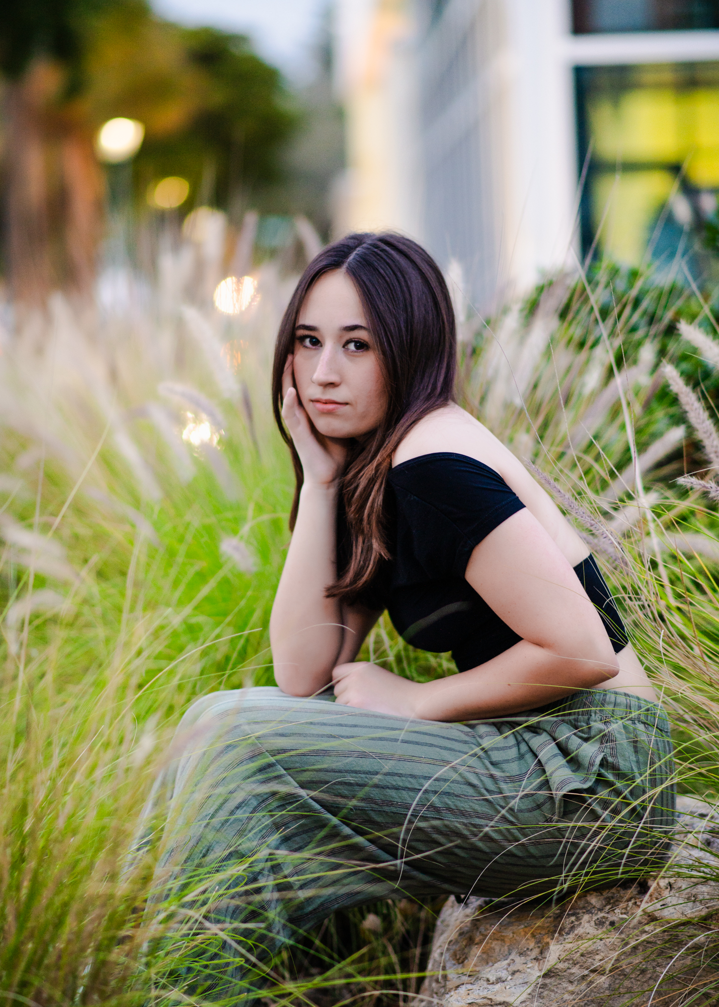 High school senior girl sitting on the rocks in tall grass for her senior portrait